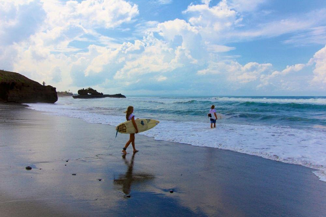 Featured image for 15-day relax pack yoga retreat in Pelan Pelan Bali with two surfers heading in to Balinese ocean to surf