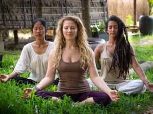 Featured image for Top 30 Yoga Retreats for November, 2017 Holiday Season with 3 female yogis in lotus pose, meditating outside on green grass at the 6-Day Integral Yoga and Meditation Retreat in Cambodia
