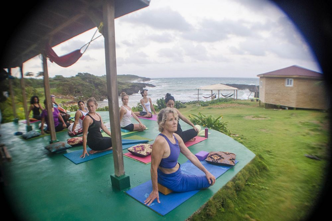 Featured image of top 30 yoga retreats for November 2017 with an outdoor female yogi class in middle of pose and the beautiful Long Bay, Jamaican ocean in the background for the 6 Day Juice Cleanse Detox, Yoga and Meditation Retreat in Long Bay, Portland Parish, Jamaica