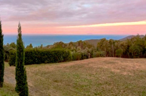 Featured image for 8-day transformation yoga retreat in Tuscany, Italy with a picture-perfect sunset colored in peach, orange, pink and light purple above an ocean blue water setting
