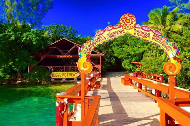 Featured image of top 30 yoga retreats for November 2017 with 8-Day Sivananda Yoga and Meditation Holiday Retreat in the Bahamas displaying crystal clear green water with royal blue sky and a deck with orange rails and an arch shaped welcome sign reading Sivananda Ashram Yoga Retreat
