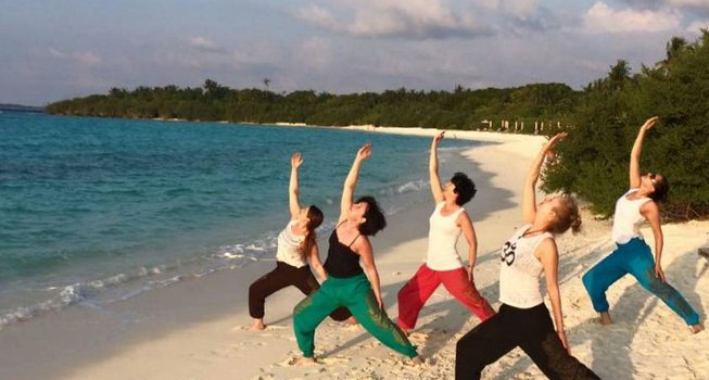 Featured image for 8 Days Yoga Retreat in Maldives with female yogis in pose at white sandy beach of Maldives island