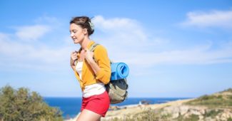 Female yoga teacher training trainee walking by the beach with yoga mat and bag on her back